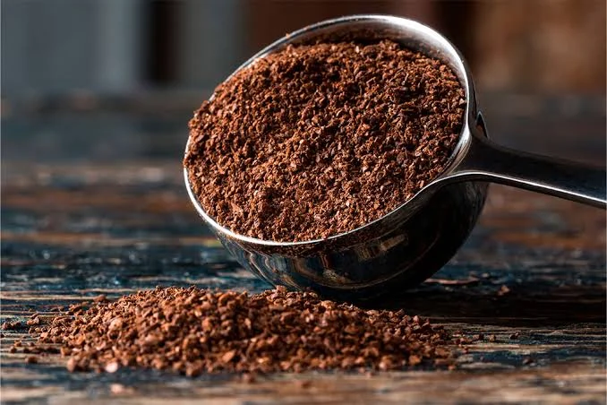 Café molido de color tostado en una cuchara de metal, sobre una superficie de madera oscura.